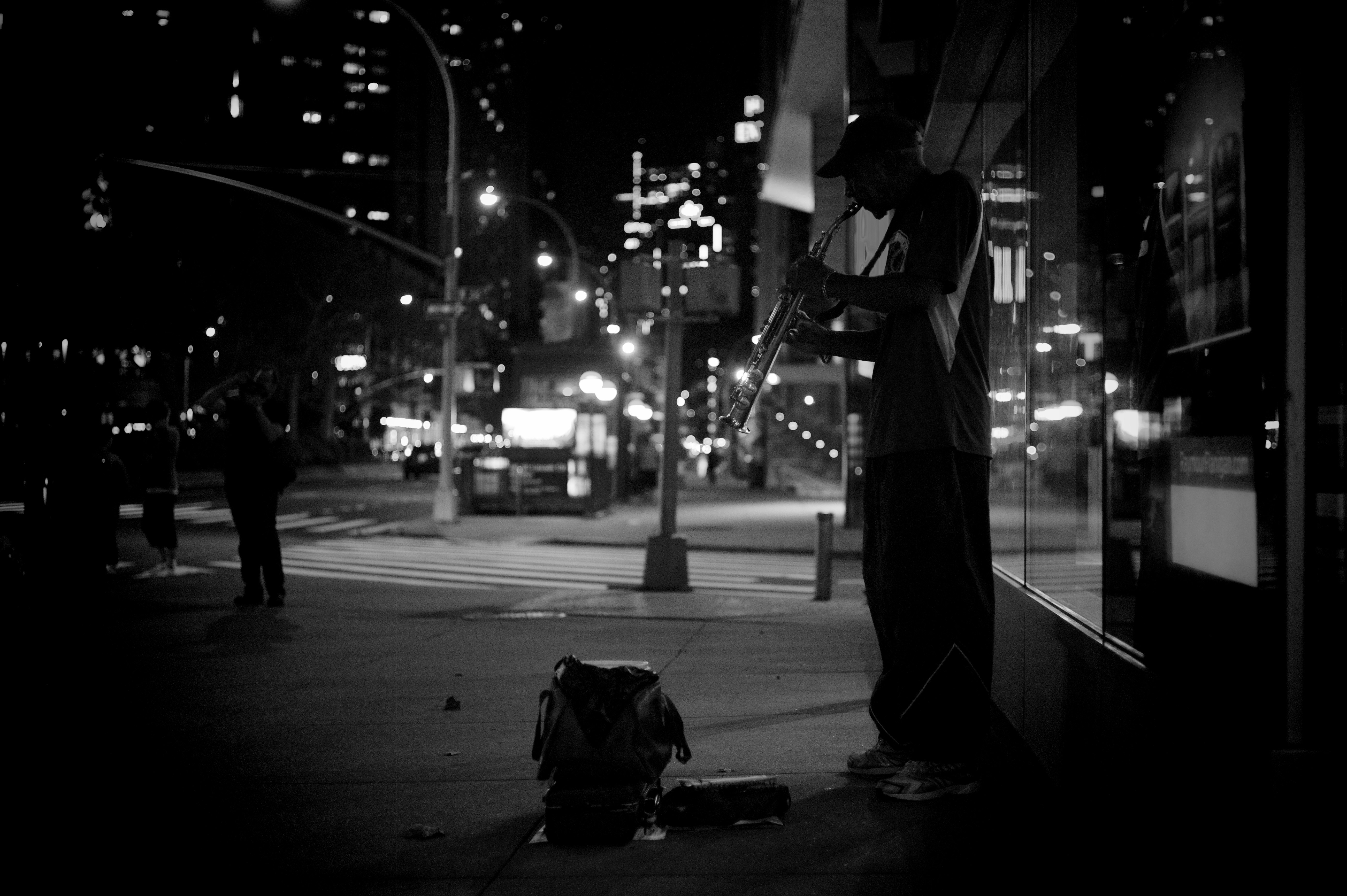 grayscale photography of man playing musical instrument beside road